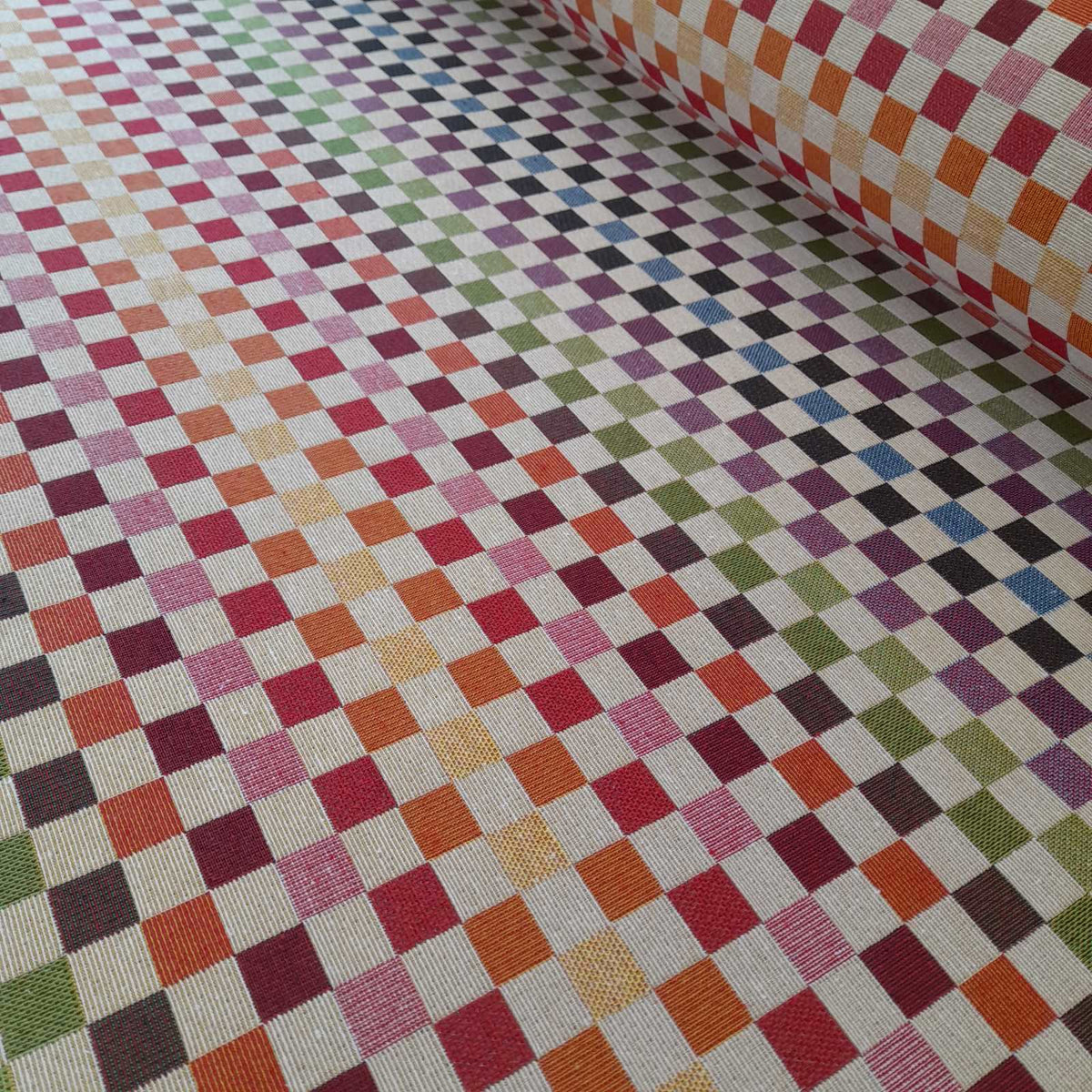 A roll of tapestry fabric with small squares in rainbow colours
