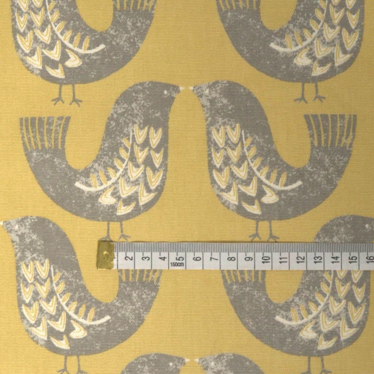 Fabric with a design of grey scandi style birds on a mustard background and a rule for scale